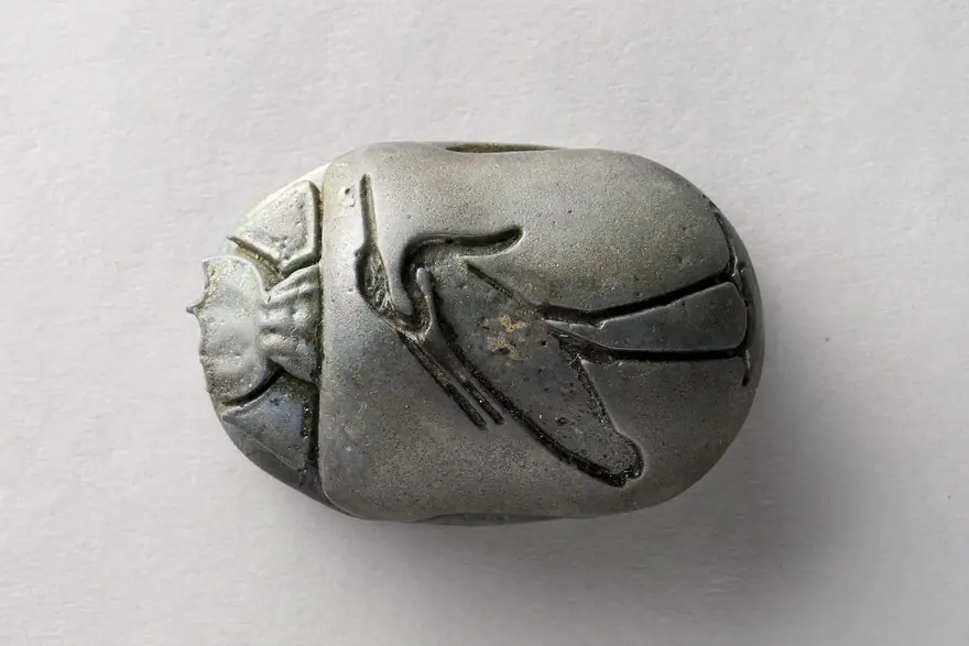 Grau-grünes Skarabäus-Amulett mit eingeritzten Flügeln auf hellem Grund